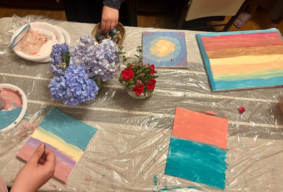 A table of sunset-striped canvases, paint plates and blue hydrangeas from a painting party